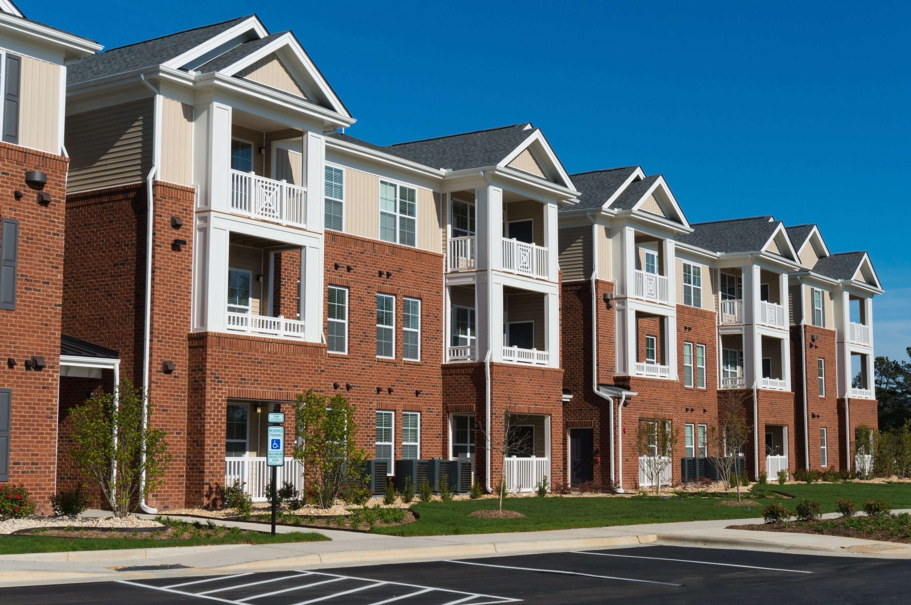 An apartment building with white decks and some parking spots in front.