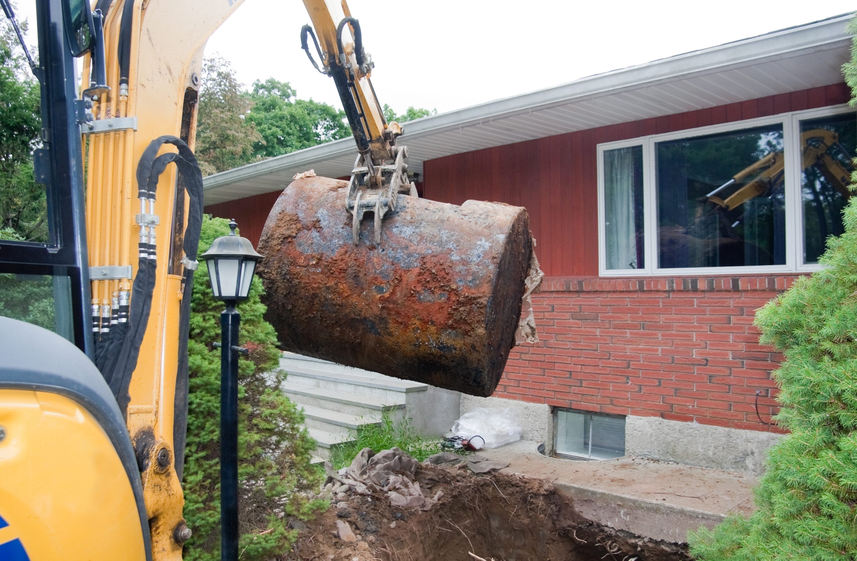 An excavator digging a hole by a brick house.