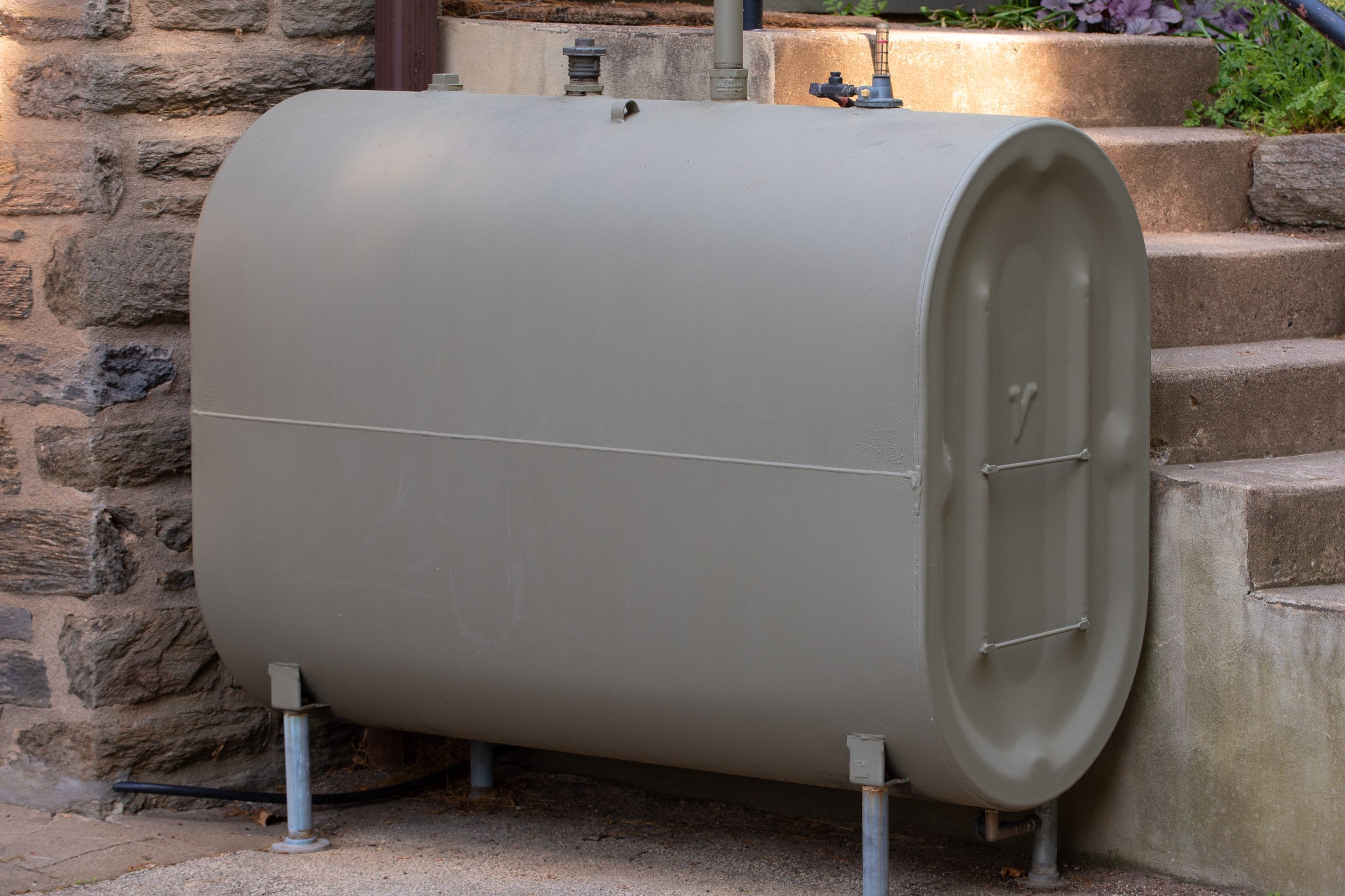A gray oil tank against a brick wall with concrete steps in the background.