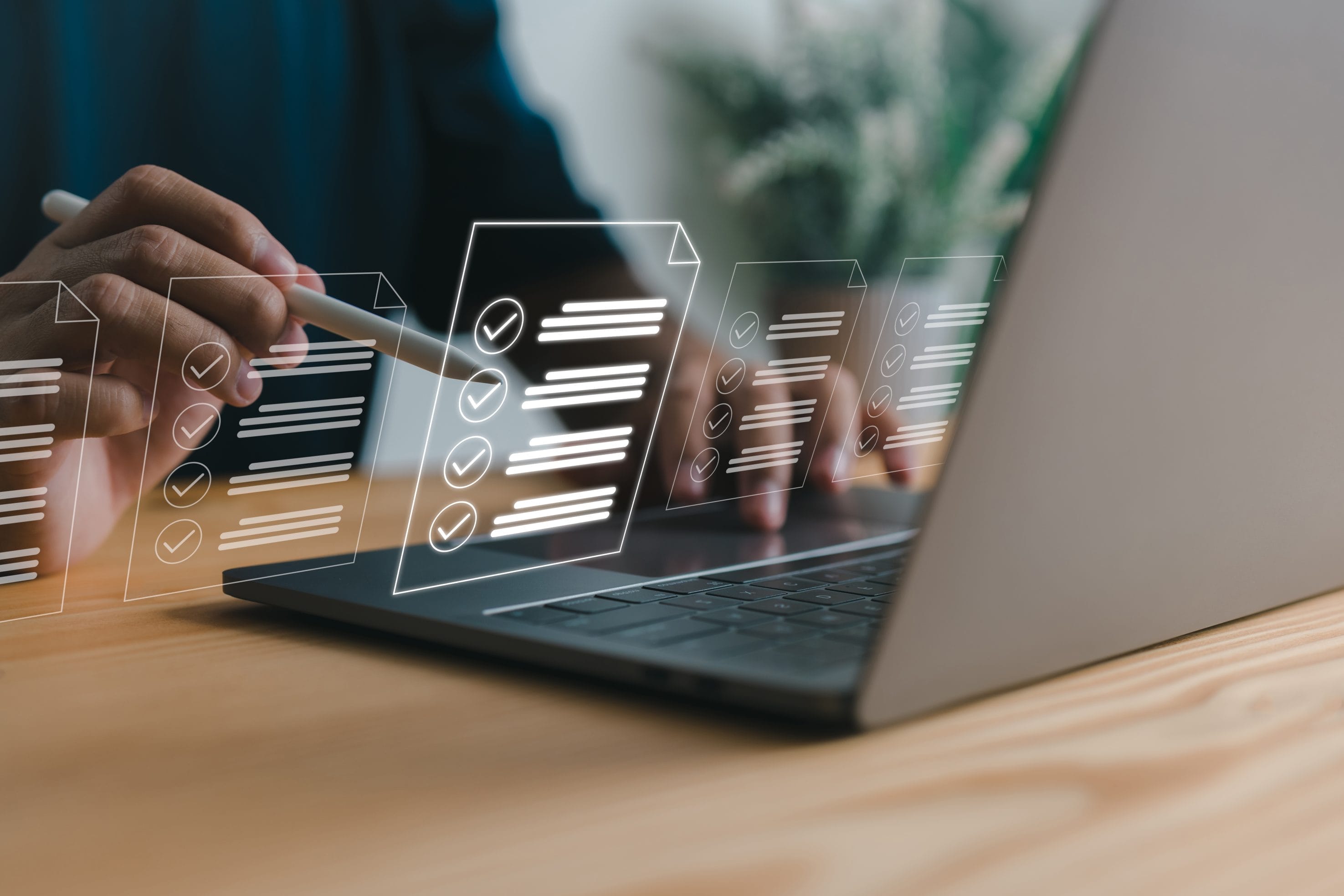 A photo of someone working on a laptop, using a pencil to point at hologram images of checklists.
