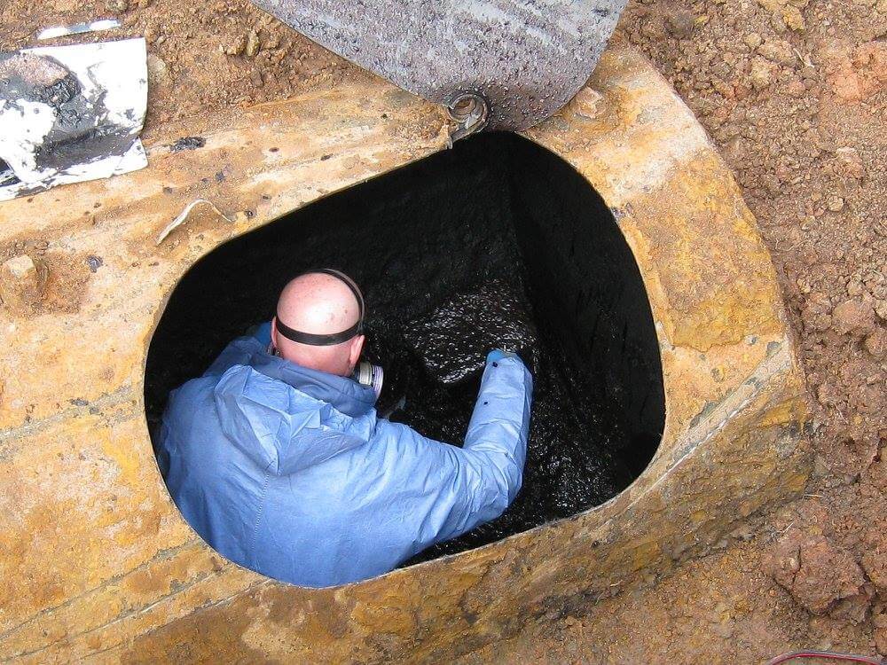 A man in blue underground in an oil tank doing environmental services.