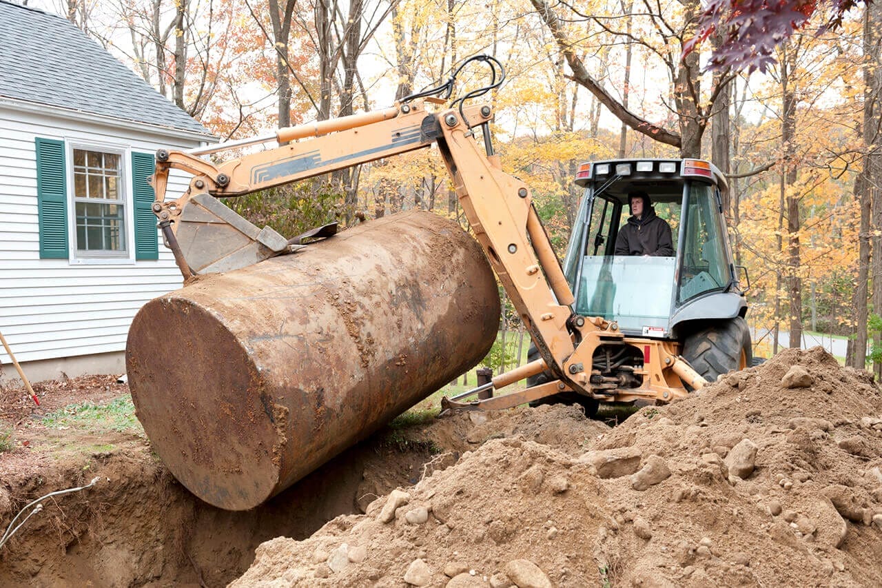 An excavator pulling out an old oil tank from a hole in someone's yard.